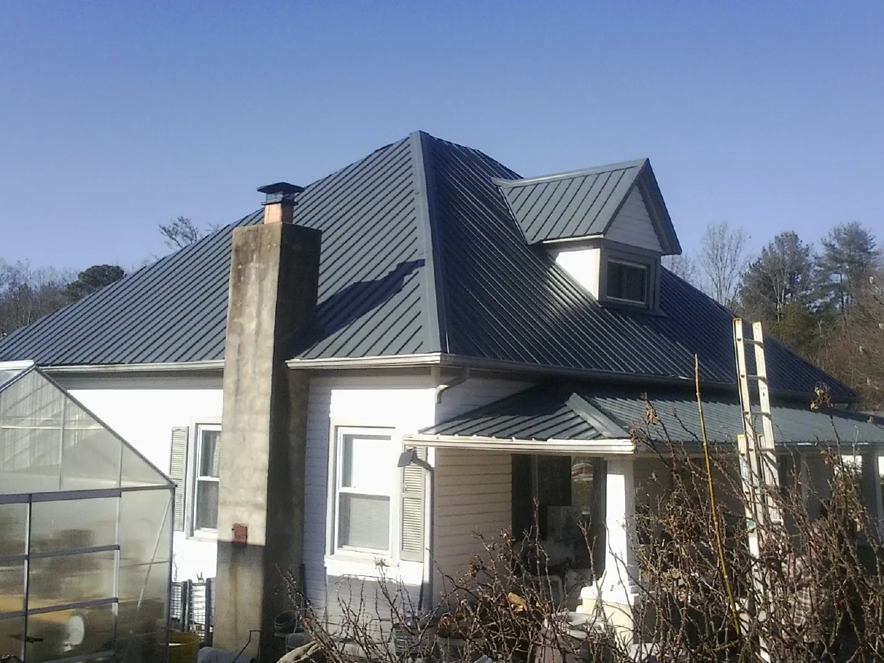 Dark blue standing seam metal roof on a white farmhouse with dormer — Slate & Tile Roof Repair by Roofing Brothers in Rockaway Beach