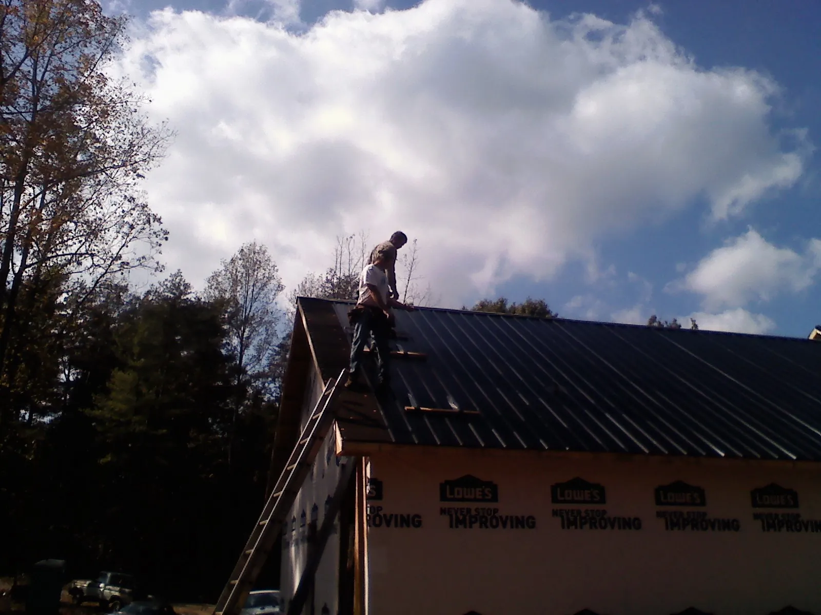 Roofer fastening dark metal panels high against a cloudy sky, from a Roof Inspection job in Rockaway Beach