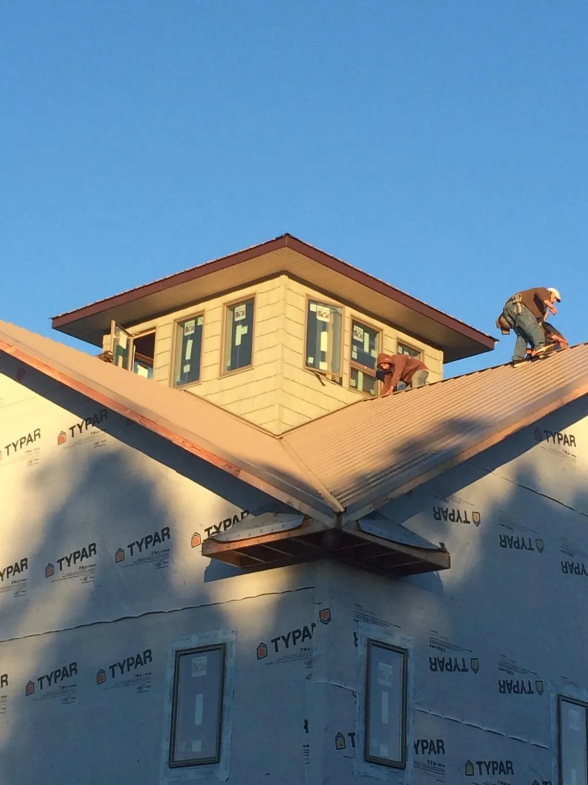 Roofers working around a rooftop cupola on a new metal roof at sunset — Roof Waterproofing in Rockaway Beach by Roofing Brothers